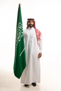 رجل سعودي بالزي التقليدي يرفع علم المملكة العربية السعودية