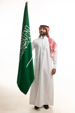 رجل سعودي بالزي التقليدي يحمل علم المملكة العربية السعودية
