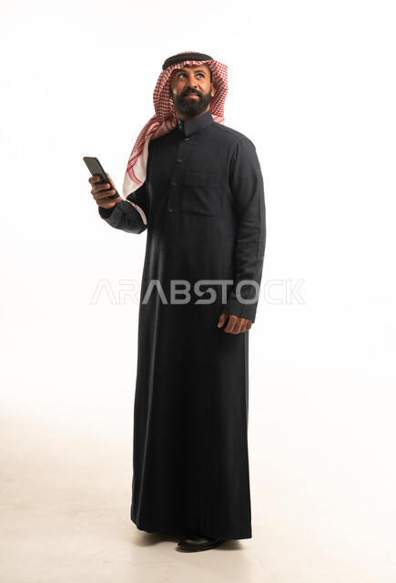 رجل سعودي بالزي التقليدي يحمل هاتفاً ذكياً