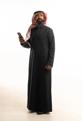 رجل سعودي بالزي التقليدي يحمل هاتفاً ذكياً