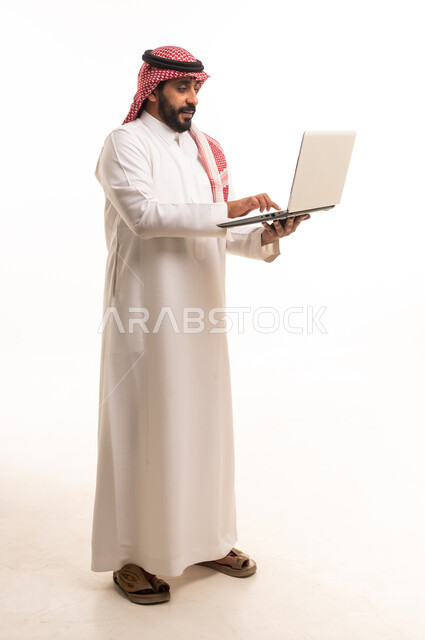 رجل سعودي بالزي التقليدي يستخدم الكمبيوتر المحمول
