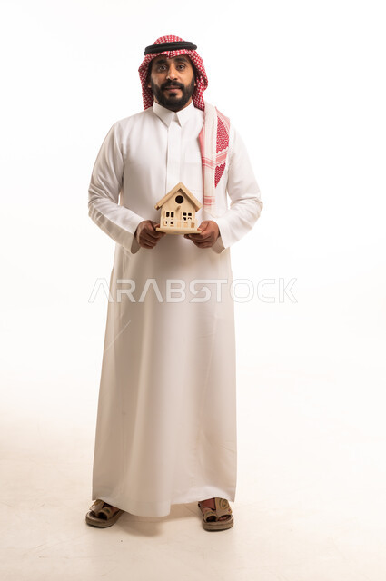 رجل سعودي بالزي التقليدي يحمل مجسم منزل