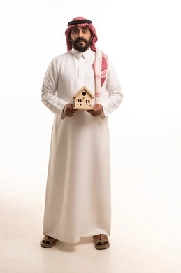 رجل سعودي بالزي التقليدي يحمل مجسم منزل