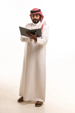 رجل سعودي يقرأ كتاباً بالزي التقليدي في استوديو
