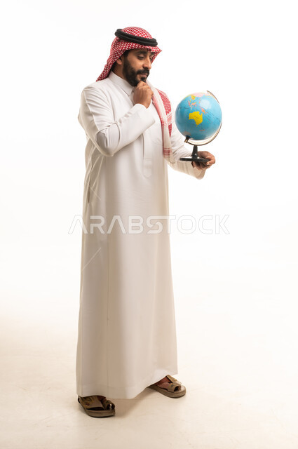 رجل سعودي يرتدي الثوب التقليدي يمسك مجسم الكرة الأرضية