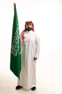 رجل سعودي يمسك بالعلم الوطني على خلفية بيضاء