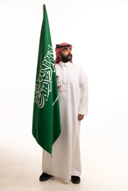 رجل سعودي بالزي التقليدي يحمل العلم الوطني