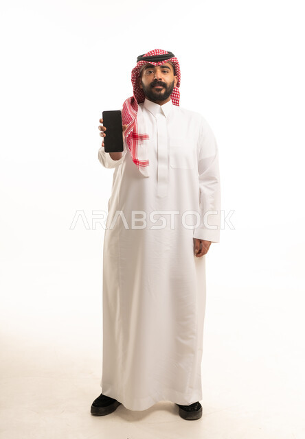رجل سعودي بالثوب التقليدي يحمل هاتفاً ذكياً