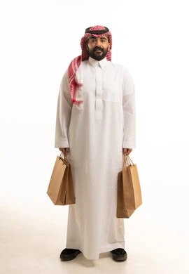 رجل سعودي بالزي التقليدي يحمل أكياس تسوق ورقية