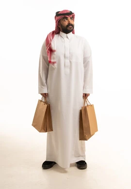 رجل سعودي يحمل حقائب تسوق ورقية بخلفية بيضاء