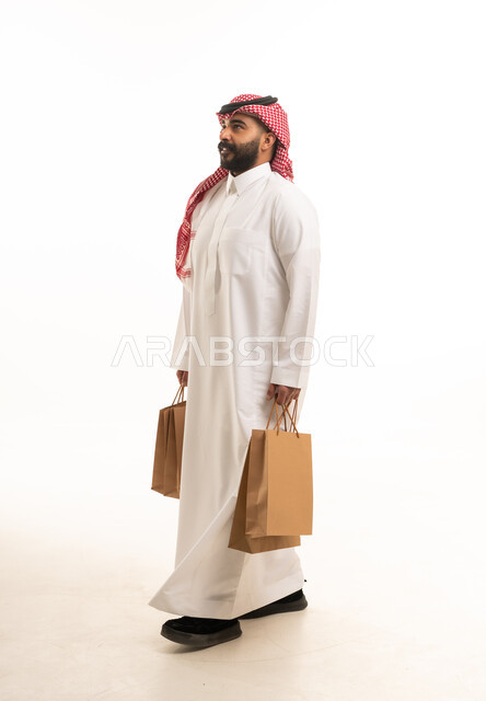 رجل سعودي بالزي التقليدي يحمل حقائب تسوق