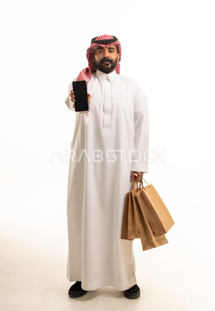 Saudi Man Holding Smartphone and Shopping Bags in Studio