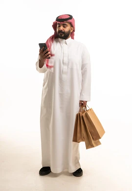 رجل سعودي يحمل أكياس تسوق وهاتف ذكي في الاستوديو