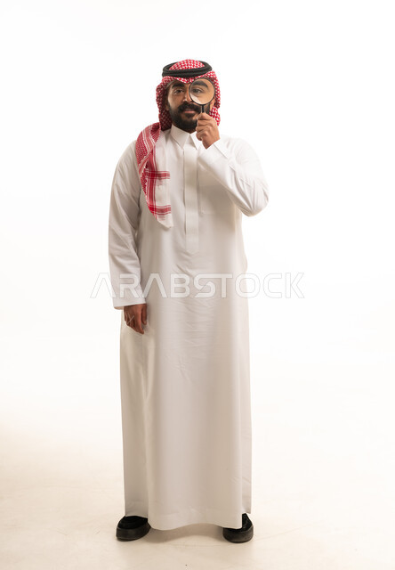 رجل سعودي بالثوب التقليدي يحمل عدسة مكبرة في الاستوديو