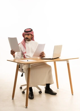 رجل أعمال سعودي يعمل على مكتبه بتعبير مندهش