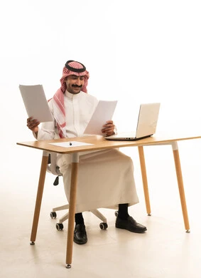 رجل أعمال سعودي مع حاسوب محمول وأوراق في الاستوديو