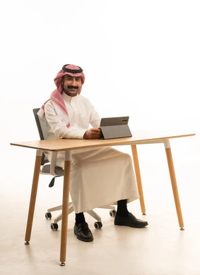 رجل سعودي يستخدم جهازاً لوحياً على مكتب عمل عصري