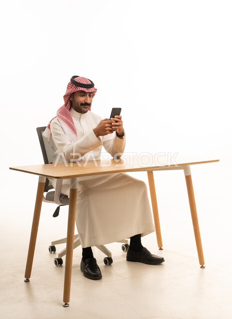 رجل سعودي بالزي التقليدي يستخدم الجوال في المكتب