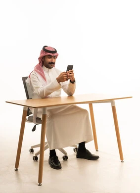 رجل سعودي بالزي التقليدي يستخدم الجوال في المكتب