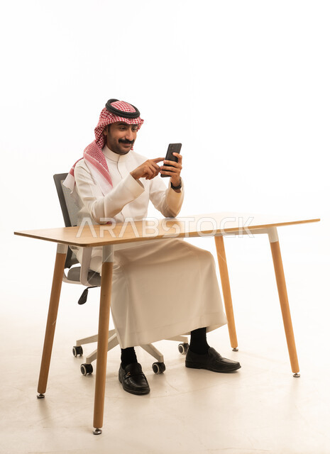 Saudi Man in Traditional Thobe Using Smartphone at Desk