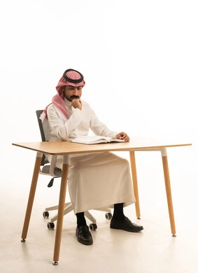 رجل سعودي بالزي التقليدي يقرأ كتاباً خلف المكتب