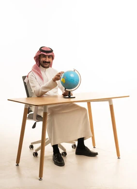 Saudi Man in Traditional Thobe with Globe at Desk