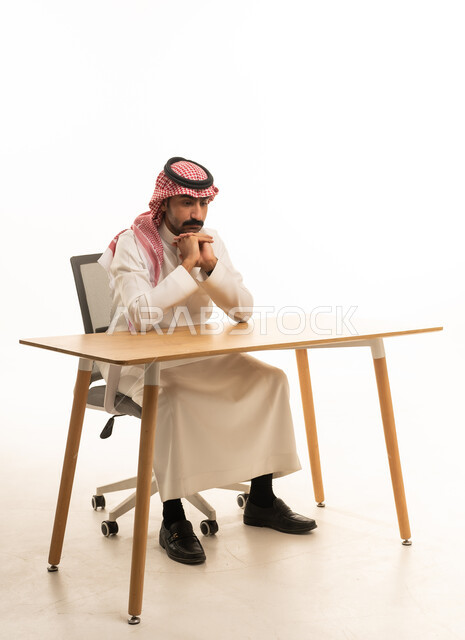 رجل سعودي بالثوب التقليدي يجلس خلف مكتب عمل