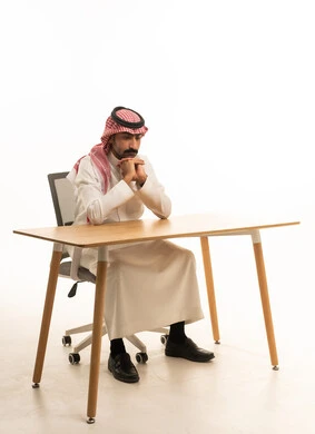 رجل سعودي بالثوب التقليدي يجلس خلف مكتب عمل
