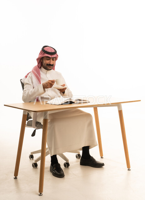 رجل سعودي بالثوب يقرأ كتاباً خلف المكتب