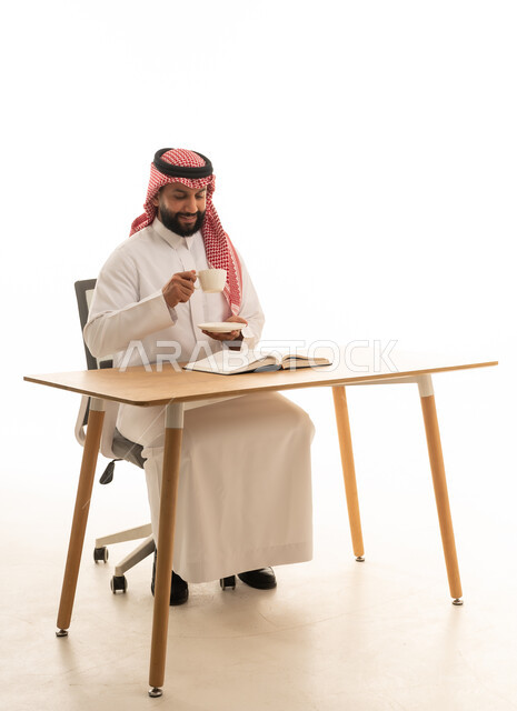 رجل سعودي بالثوب التقليدي يقرأ على مكتب عمل