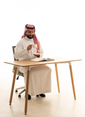 رجل سعودي بالثوب التقليدي يقرأ على مكتب عمل