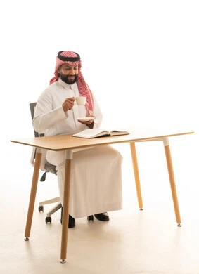 Saudi Man in Traditional Dress Reading Book at Desk