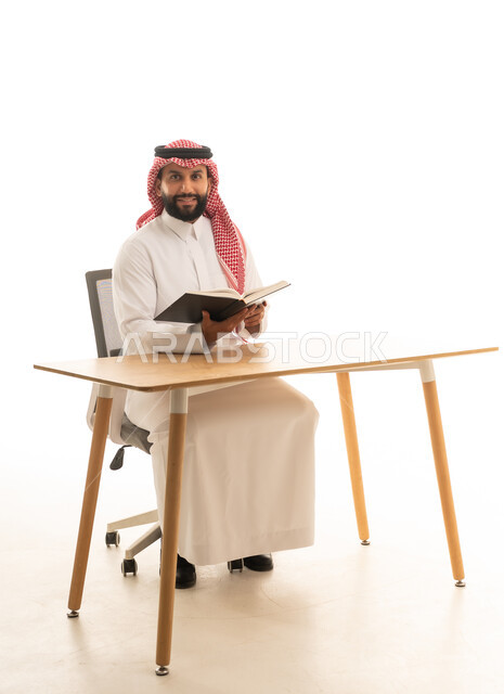 رجل سعودي يقرأ كتاباً على مكتب بخلفية بيضاء