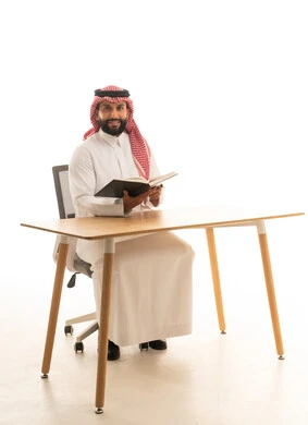 Saudi Man Reading Book at Desk on White Background