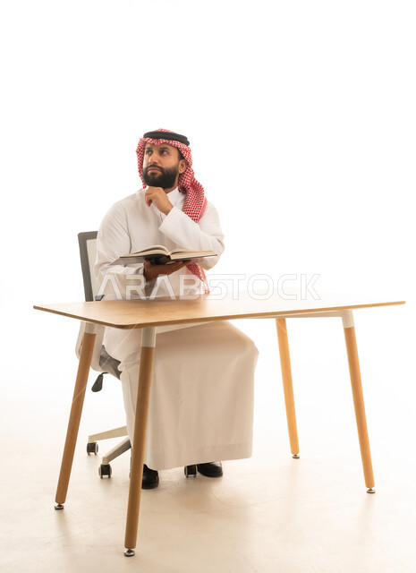 رجل سعودي بالزي التقليدي يقرأ على المكتب