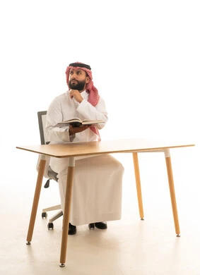 رجل سعودي بالزي التقليدي يقرأ على المكتب