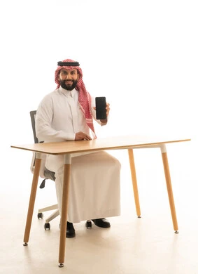 Saudi Man in Thobe Holding Smartphone at Office Desk