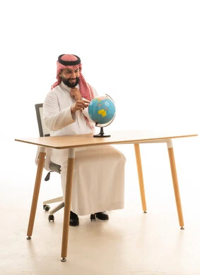 Saudi Man in Traditional Thobe with Globe at Desk