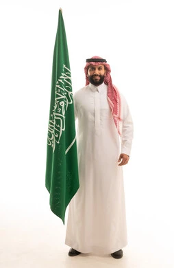 رجل سعودي بالزي التقليدي يمسك علم المملكة