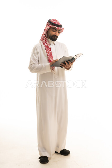 رجل سعودي بالزي التقليدي يقرأ كتاباً في الاستوديو