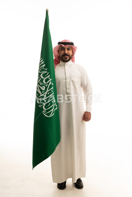 رجل سعودي بالزي التقليدي يحمل العلم الوطني