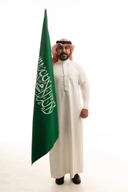 رجل سعودي بالزي التقليدي يحمل العلم الوطني