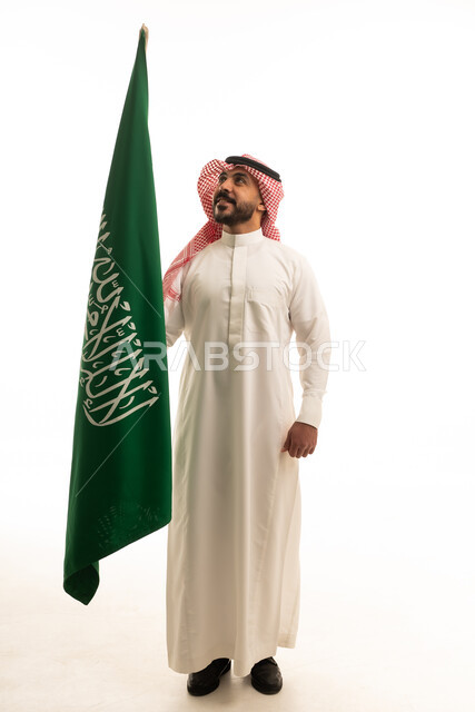 رجل سعودي يحمل علم المملكة العربية السعودية بخلفية بيضاء