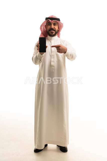 رجل سعودي باللباس التقليدي يشير إلى هاتف ذكي
