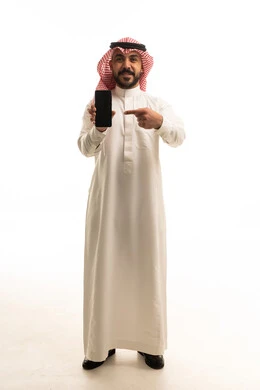 رجل سعودي باللباس التقليدي يشير إلى هاتف ذكي