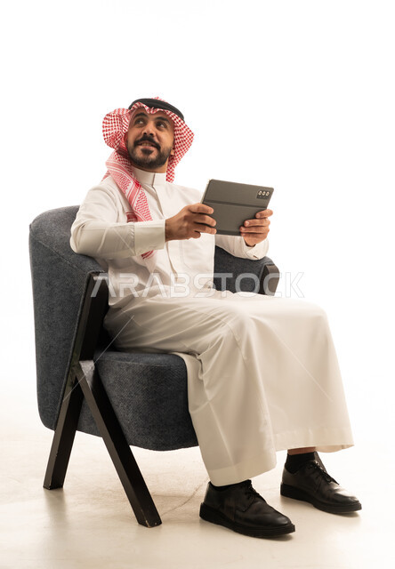 رجل سعودي بالزي التقليدي يمسك جهاز لوحي بخلفية بيضاء