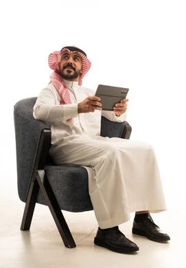 رجل سعودي بالزي التقليدي يمسك جهاز لوحي بخلفية بيضاء