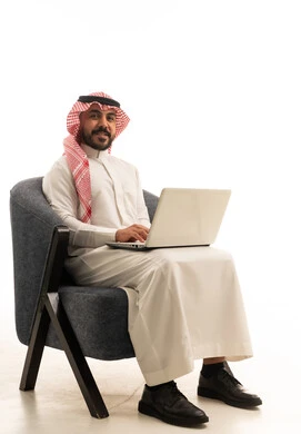 رجل سعودي بالزي التقليدي يستخدم جهاز كمبيوتر محمول