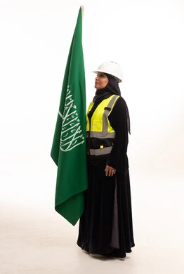 مهندسة سعودية مع العلم الوطني بملابس السلامة