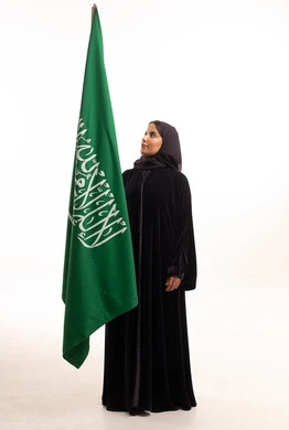 امرأة سعودية بالعباءة السوداء مع علم المملكة العربية السعودية